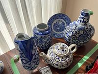 Lot of blue pottery items on a wooden surface near window, showing vases, jar, plate, and teapot in blue and white ceramic patterns