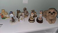 Photo showing nine assorted collectible figurines including Cherished Teddies bears and a small dog figurine
