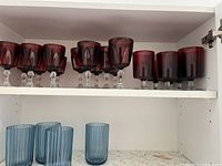 Red and blue glasses arranged on two shelves inside a cabinet. The top shelf has red glasses in multiple styles; the bottom shelf has blue plastic drinkware.