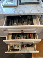 Three kitchen drawers open showing organized cutlery and utensils inside with plastic trays.