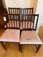 Four matching wooden dining chairs with vertical slat backs and pink damask upholstered seats, all placed on a wood floor against a wall.