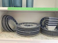 View showing stacked dinner plates, side plates and bowls on a shelf with visible blue floral pattern.