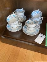 Photo showing twelve cups stacked in three groups on their matching saucers with blue and turquoise leaf floral patterns and gold edging.