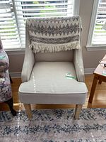 Front view of beige upholstered occasional chair with decorative throw draped over the back.