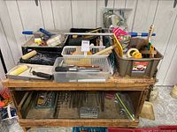Overview of multiple painting tools and supplies on a wooden table showing paint rollers, trays, brushes, scrapers and bins.