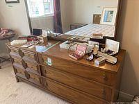 Front view of the wooden dresser with six drawers and jewelry on top, mirror reflecting the room.
