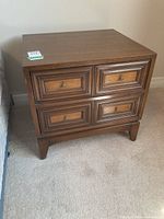 Wooden side table with two drawers and brass knob handles shown from the front on beige carpet.