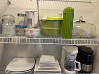 Kitchen shelf with various kitchen items including dishes, coffee makers, and storage containers.
