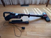 Full length view of vacuum cleaner with extension wand, crevice/brush tool, power charger on wood floor under sunlight.