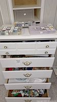 Multiple drawers open containing plastic containers with embroidery floss wound on cards, embroidery hoops, and fabric bundles.