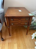 Side view of wooden side table showing two drawers with metal ring pull handles and legs with carved detailing.