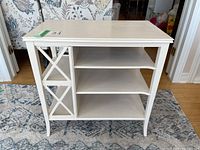 Front view of white painted side table showing shelves and cross detail on left side