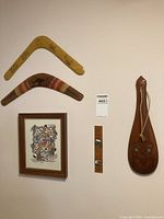 Photo of two boomerangs, framed Aboriginal art print, carved wooden wall hanging with face, and leather strip with mounted objects on a wall.