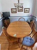 Full view of oak oval dining table and six matching chairs around it, showing wood grain and some chairs with blue cushions.