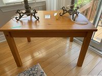 Front view of wooden side table showing rectangular top and four legs on hardwood floor near window