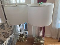 Two matching table lamps displayed on wood table beneath windows.