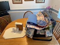 View of table displaying various linens and dining accessories including placemats, napkins, and a ceramic dish, with some items stacked.