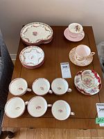 Photo showing 5 teacups and 10 saucers, some with floral patterns and colorful accents placed on a wooden table.