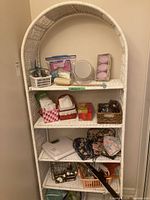Wider view showing the full white wicker shelving unit with five shelves, containing various small items (not included).