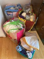 Three reusable bags filled with yarn and wool remnants of various colors and thicknesses placed on floor next to furniture, with some fabric pieces rolled up nearby.