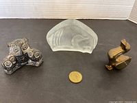Three animal figure sculptures displayed on table: carved stone owl trio, frosted glass loon, and brass bird.