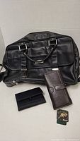Photo shows Kenneth Cole black leather computer bag with buckle straps, handles, accessories and the two wallets, brown leather Roots wallet and black cloth wallet with tag.