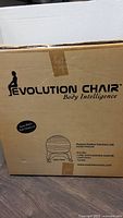 Close-up of the cardboard box showing Evolution Chair branding and product illustration of the chair with ball and pump.
