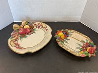 Two Fitz and Floyd ceramic plates on black background showing raised colorful fruit details and gold trim