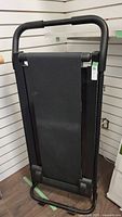 Side profile photo of the folded treadmill showing the black padded handlebar and textured walking belt in upright position.