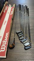 Photo showing 9 Jack Nicklaus Golden Bear golf clubs alongside Wilson box.
