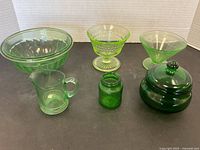 Various vintage green glass bowls and containers arranged on black surface.
