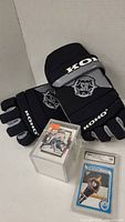 Pair of black Koho hockey gloves with gray palms and gray logos, along with a sealed box of hockey cards and two hockey cards in protective cases including Wayne Gretzky rookie card.