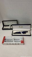 Overview of three boxed pen sets by Cross, Pierre Cardin, and Bill Blass showing packaging and pens inside.