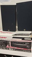 Pair of black Wharfedale CRS-3 speakers positioned on box of Pioneer VSX-917V-K receiver showing front grilles and box front