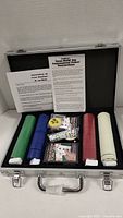 Poker set in open aluminum case showing stacks of poker chips in green, blue, yellow, red, and white, two decks of cards, five dice, and an instruction booklet.