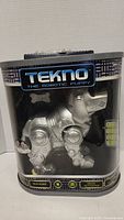 Front view of Tekno robotic puppy in clear display packaging with brand and main features visible.