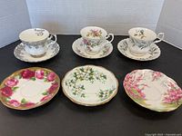 Three Royal Albert tea cups each with matching saucers, plus three extra saucers laid out on black surface with white backdrop