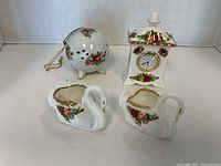Porcelain clock with floral rose pattern, potpourri ball, and two swan figurines arranged on white background.