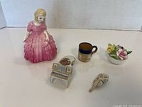 Overview of the lot showing the Royal Doulton Rose figurine, miniature piano and violin, floral china arrangement, and small ceramic mug