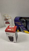 Photo showing two Stella Artois beer glasses with clear glass and gold rims along with two boxed Tsunami handle tumblers shaped like camera lenses.