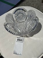 Clear Brilliant Period cut glass bowl with deep cut geometric and fan patterns, scalloped rim, displayed on a white circular surface outdoors in sunlight.