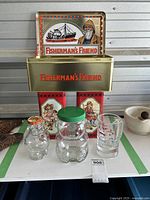 View of the full lot showing all collectible tins and glass jars including the Fisherman's Friend tin, Premium Plus tins, bear-shaped glass jars, penny jar and Carnaval glass
