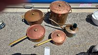All items in the lot displayed outdoors on asphalt, showing copper pots and watering can with age wear and patina.