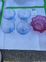 Top-down view of four blue glass dessert bowls and one cranberry glass bowl arranged on a white paper towel outdoors.