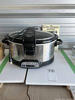 Full view of Hamilton Beach slow cooker on white surface with power cord and Slow Cooker Savers recipe booklet behind it.