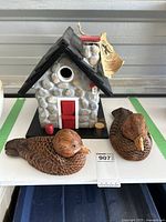 Image showing the Country Nests Windy Ridge bird house with stone texture, red door and chimney, and two Hilton carved wooden ducks in front.