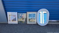 Four items pictured outside against blue door: white wicker oval mirror and three framed artworks in various frames and sizes.