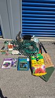 Full overview of gardening tools, hoses, books, soil bags, gloves and accessories laid out outside on pavement.