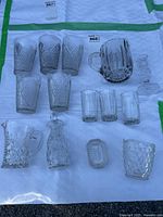 Overview of all items including multiple glasses, pitchers, vinegar jar, and candle holder arranged on white cloth.