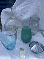 Set of 5 glass items on white quilt background including 2 clear vases (one tall bottle-shaped and one bowl with lid), 2 blue glass vases of different shapes, and the lid separate on the side.